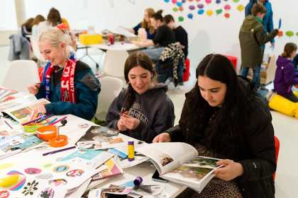 Three women sat at a table covered with art materials and books.