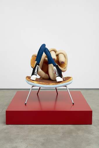 Seated Sarah Lucas sculpture on a square red plinth