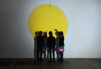 A group of students stand in front of a projection of a large yellow circles.