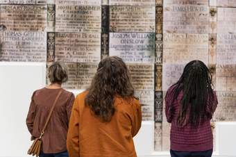 A group of three teachers with their backs to the camera, looking at a text-based artwork on the wall of Tate Britain.