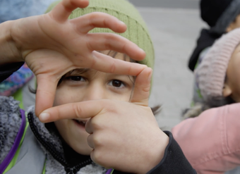 A boy looks through his fingers at the camera