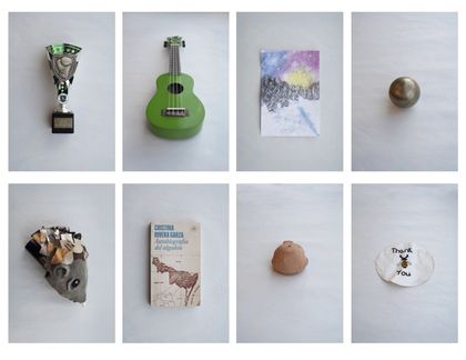 Photo of a series of 8 objects: a small boxing trophy, a green ukulele, a drawing of a forest in the winter, a brass ball, a hedgehog with fabric pieces instead of spikes, a book, a tiny clay figurine of a fish, and a bee