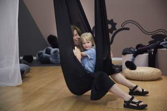 A child and adult laughing and playing in a large, black fabric sensory swing