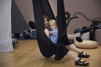 A child and adult laughing and playing in a large, black fabric sensory swing