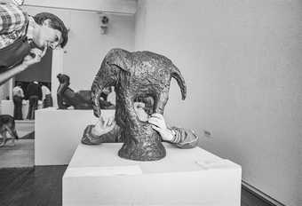 A child handles Barry Flanagan's bronze sculpture of an elephant. To his right, another visitor leans into view to survey the scene.