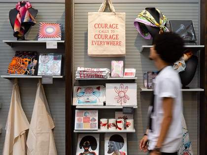 A person walking through an art gallery shop with prints, tote bags and scarves
