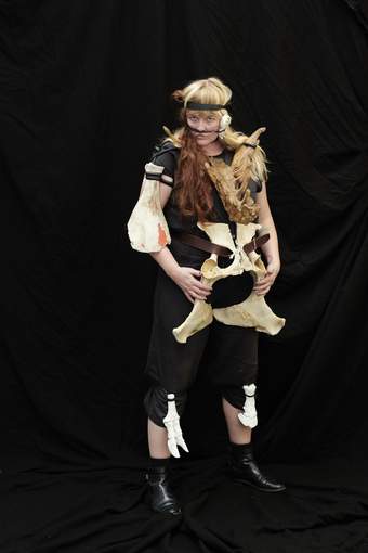 A person wearing black with animal bones strapped to their body