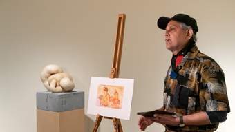 A visitor standing in front of a sculpture and an easel displaying another artwork.