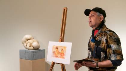 A visitor standing in front of a sculpture and an easel displaying another artwork.