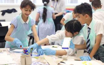 A photograph of 3 schoolchildren printing at a table