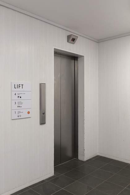 A tall silver lift with an information board listing the floors accessible by this lift: the first, third and fourth floors.