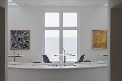 A round table with two chairs at a window overlooking the sea.
