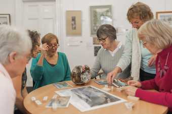 A group of 6 different women grouped around a table studying a sculpture and photograph.