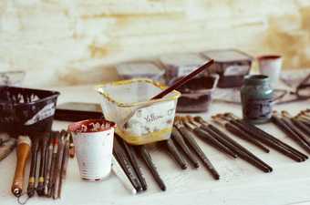 A selection of paint brushes and pots of pigment, including one labelled yellow ochre