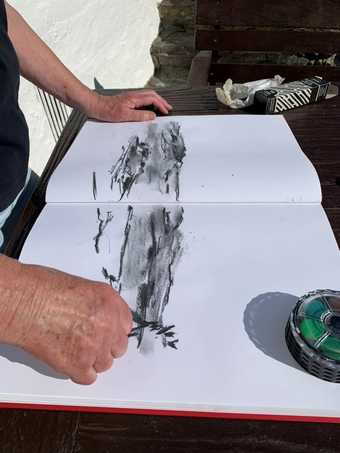 A hand drawing in an open sketchbook with a small black sketch of the landscape created using charcoal