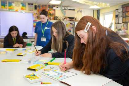 Students sit at a table in a classroom whilst drawing