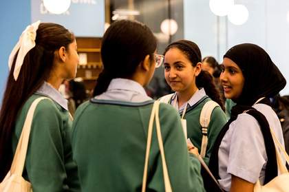 Four young people speaking to each other. The two in the foreground face away from the camera and towards the other two. We can see the backs of their green jumpers.