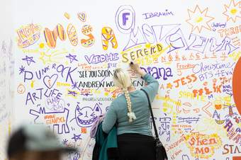 A photograph of a visitor drawing a message on a white wall.