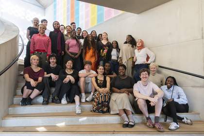 Tate Collective Producers on a staircase at Tate Modern smiling at the camera, some are standing and some sitting at the front