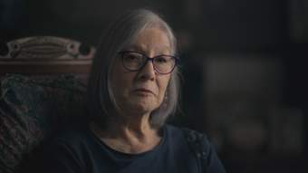 'Close up shot of an older mixed British and Chinese woman, with grey hair and glasses, wearing a navy blue top.