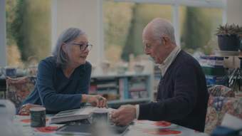 An older couple sit at a table, looking at a family photo album.