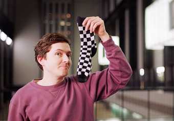 A man sniffing a black and white sock looks at the camera