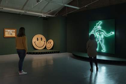 2 visitors stand looking at a neon artwork