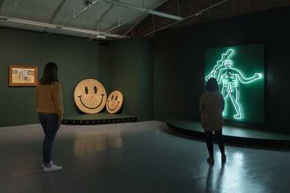 2 visitors stand looking at a neon artwork