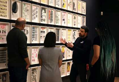 John, one of Tate Liverpool's Visitor Engagement Assistants, points to an artwork whilst talking with a small group of visitors