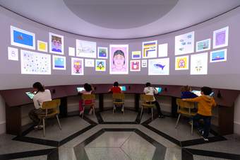 Children drawing on digital screens with digital artworks appearing on the walls of the large curved room