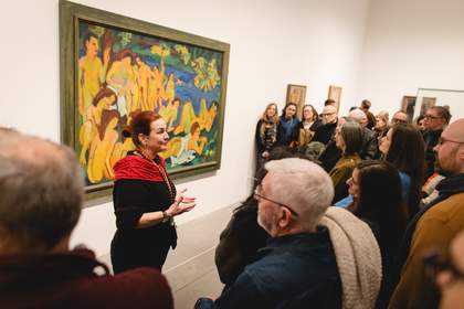 A person standing in front of a painting giving a talk to a group