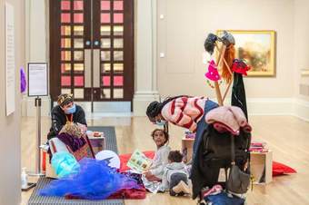 A family is inside the gallery, children are dressed up in fairytale costumes whilst being read a story