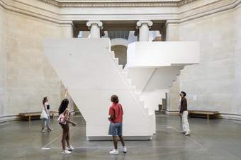 People looking at an artwork that is a large white cast of a staircase