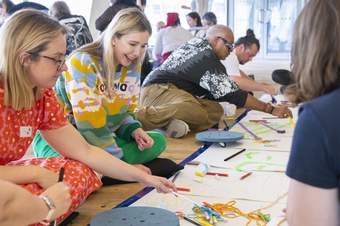 A group of teachers working on a collaborative floor drawing.