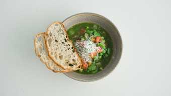Earthenware bowl of vegetable soup with a slice of bread balanced on the edge.