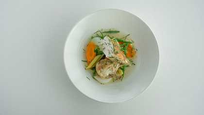 Two pieces of fish in a white bowl with some sliced vegetables underneath.