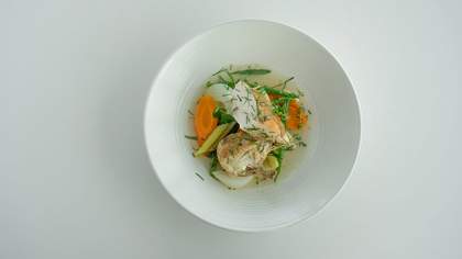 Two pieces of fish in a white bowl with some sliced vegetables underneath.