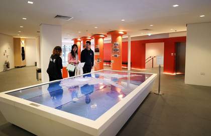 A photograph of visitors and a Visitor Engagement Assistant at Tate Liverpool + RIBA North looking at a model map displayed on a white display cabinet.
