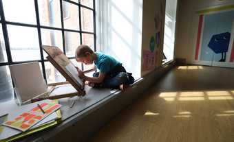 Little boy drawing at an easel by the window in Tate Liverpool's Clore Studio