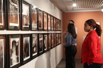 A photograph of a visitor in a red jacket looking at photographs displayed on the walls at Tate Liverpool + RIBA North.