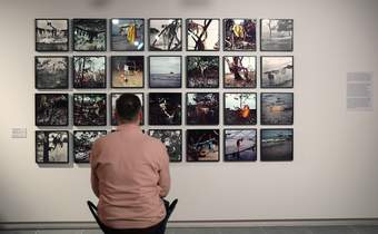 A photograph of a visitor sitting on a portable stool in front of some photographs