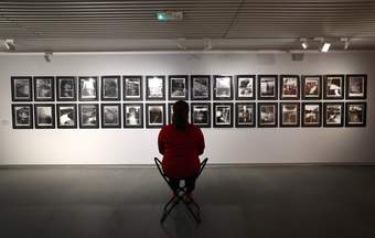 A photograph of a visitor sitting on a portable stool in front of some photographs