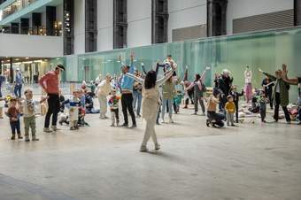 A group of children and adults, some with their arms in the air, playing in the large Turbine Hall.