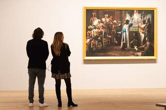 Two people looking at an artwork in a gold frame on a white wall