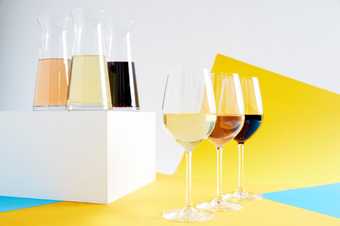 Glasses of red and white wine and a pitcher of wine against a white and yellow background