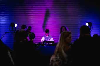 a DJ smiles whilst playing a set in a busy dark room