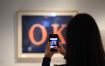 A photograph of someone taking a photograph of an artwork with the word 'OK' on it.