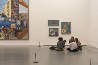 Teachers sitting on the floor in a gallery display having a conversation surrounded by artworks