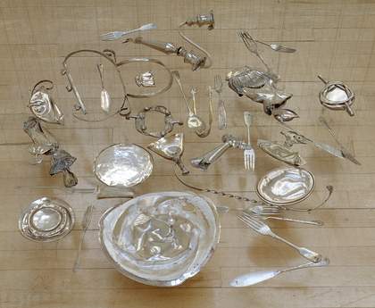 Squashed silverware arranged to lay flat in a pool, suspended just above the ground.