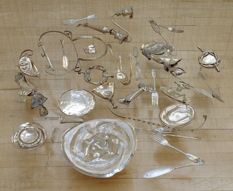 Squashed silverware arranged to lay flat in a pool, suspended just above the ground.